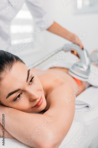 beautiful woman on massage table getting electrical massage done by cosmetologist in spa salon