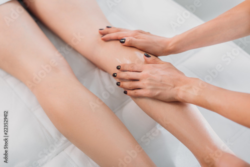 cropped shot of cosmetologist massaging clients legs in spa center