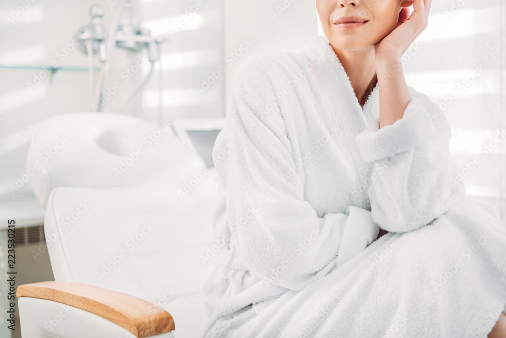 partial view of woman in white bathrobe sitting on massage table in spa salon partial view of woman in white bathrobe sitting on massage table in spa salon