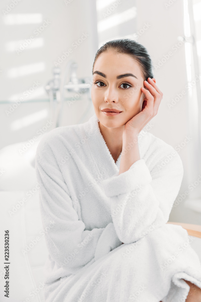 portrait of beautiful woman in white bathrobe sitting on massage table in spa salon portrait of beautiful woman in white bathrobe sitting on massage table in spa salon