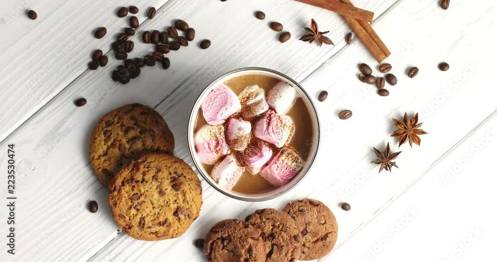 Top view of arranged white mug filled with cacao and sweet pink marshmallows on table with cookies and aromatic spices