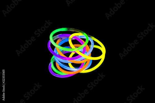 Colorful fluorescent light neon glow stick bracelet strap wristband on mirror reflection black background photo