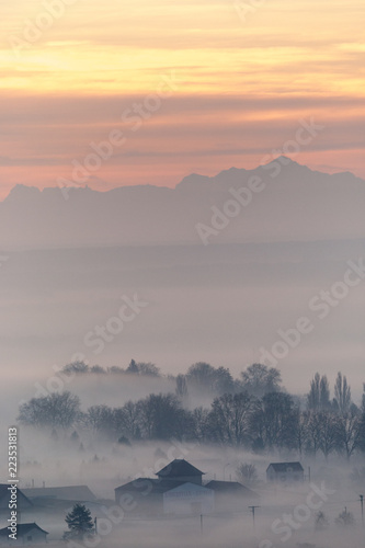 Misty trees and building with mountains and sunrise in the background
