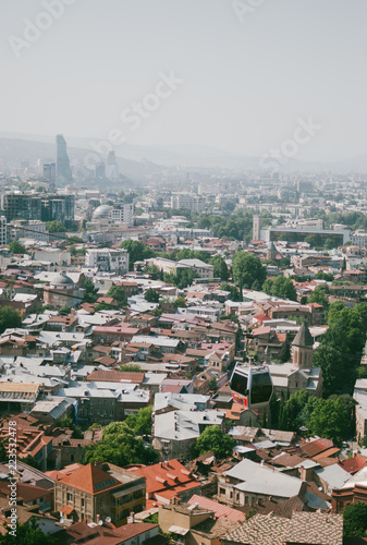 Panoramic view of Old Tbilisi, the capital of Georgia. Cable car over the city. Hot sunny afternoon. Red rooftops of old houses.