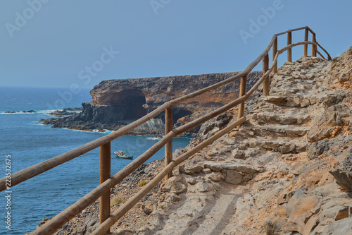 Views from the wooden staircase of a lookout with a boat sailing in the sea and the Cuevas de Ajuy in the background in Fuerteventura  Canary Islands  Spain