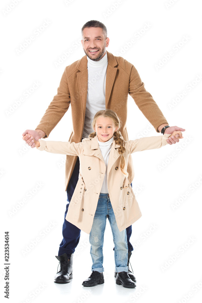 Fototapeta premium father and daughter holding hands and posing in beige coats, isolated on white