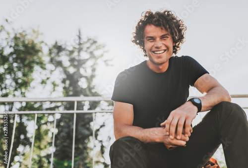 Low view shot of happy stylish young man wears black t-shirt and wirstwatch on the street. Happy smiling man posing for advertisement with copy space, outdoor in the city street. People concept