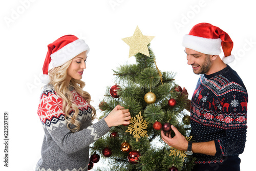 beautiful couple in santa hats decorating christmas tree, isolated on white