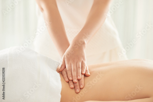 Anonymous massage therapist pressing loin of female client while working in nice massage salon