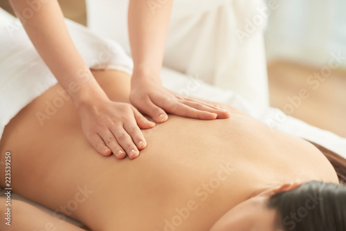 Crop hands of therapist massaging back of unrecognizable female client in spa salon