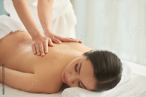 Unrecognizable massage therapist rubbing back of beautiful lady while working in spa salon