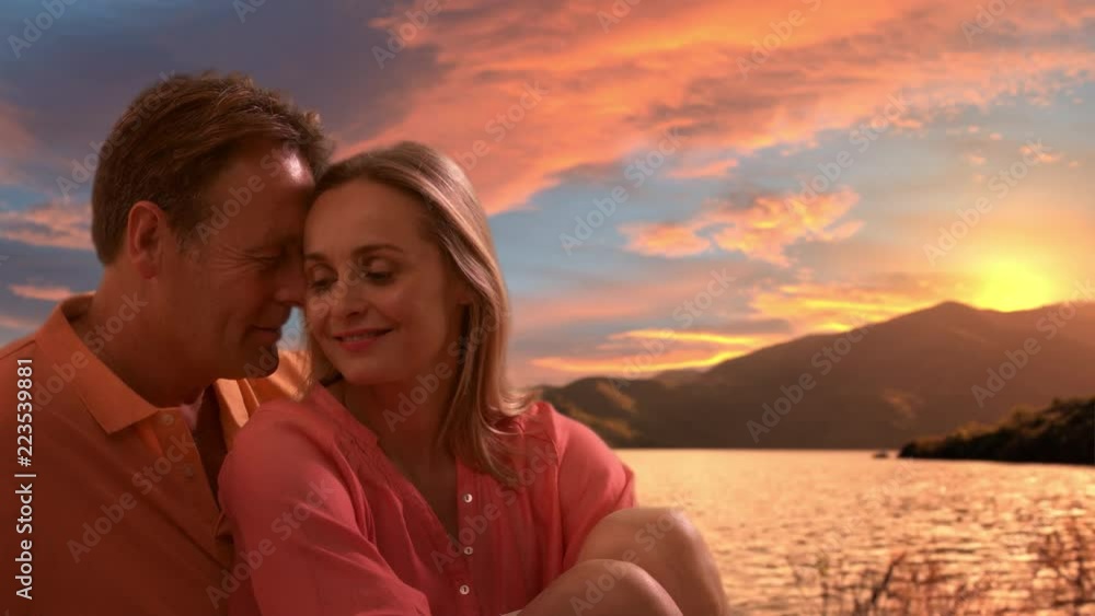 Mid aged couple in sitting looking over lake in sunset Mid aged couple in sitting looking over lake in sunset