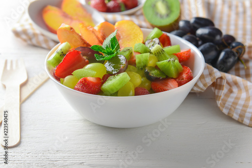 Bowl with delicious fruit salad on white wooden table
