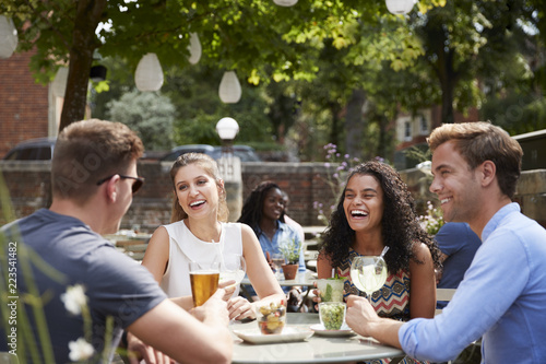 Friends Sitting At Table In Pub Garden Enjoying Drinks Together