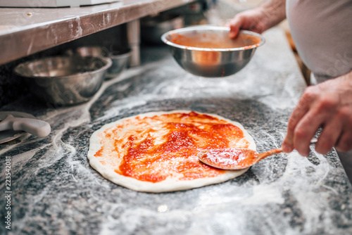 Close-up image of chef preparing the pizza base with tomato sauce.