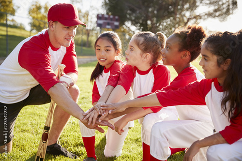 Girl baseball team kneeling with their coach, touching hands photo