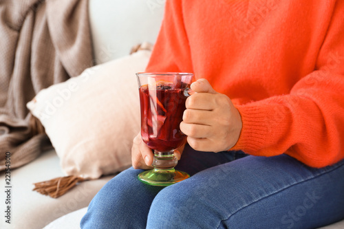 Woman holding glass cup of delicious mulled wine while sitting on sofa