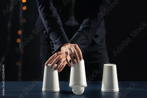 Wall Mural Magician showing tricks with cups on dark background