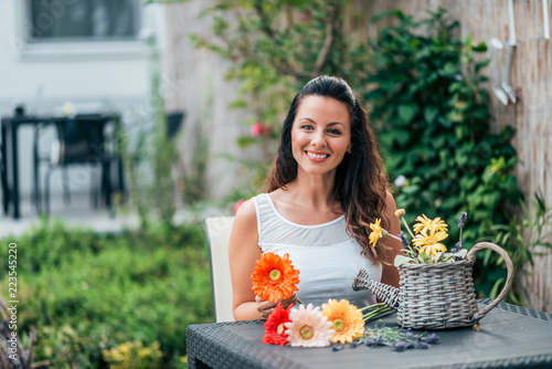 Portrait of a young woman sitting at wooden table and aranging a flower bouquet. photo