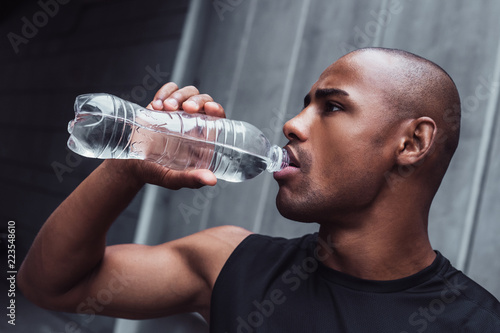 Perfect drink is always water. Portrait of handsome young man in sportswear drinking water