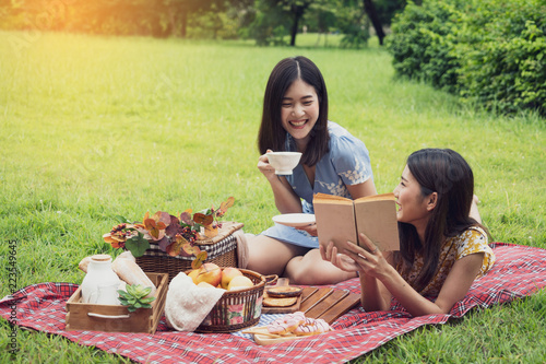 Couple of girls going picnic in a park, reading a book together and feeling friendly.