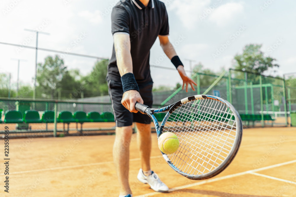 Close up of man holding racket at right hand and beating a tennis ball.