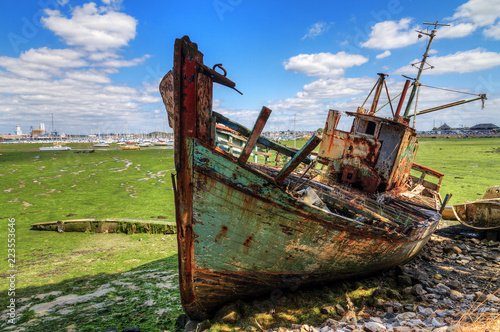 Old rusty fishing boat wreck on green dry land at low tide in the harbour of Larmor-Plage, Lorient, France, in summer