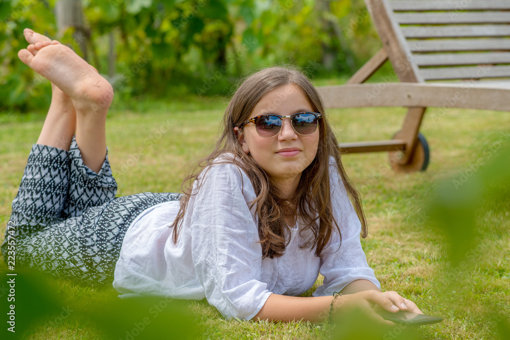 beautiful young girl with sunglasses lying on the grass using a smartphone
