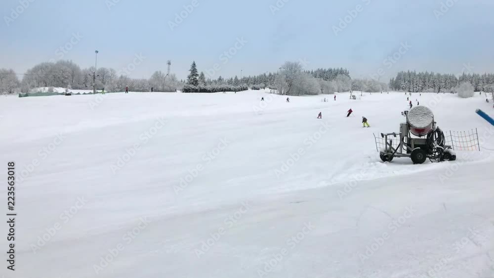 People skiing downhill on snow slope in winter ski resort. Snow canon on ski mountain near children and adults ski trail. Winter activity with skiers riding down on piste at winter day People skiing downhill on snow slope in winter ski resort. Snow canon on ski mountain near children and adults ski trail. Winter activity with skiers riding down on piste at winter day