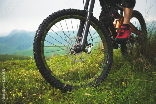 Close-up of a mountain bike wheel in the mountains on the green grass and foot of a rider