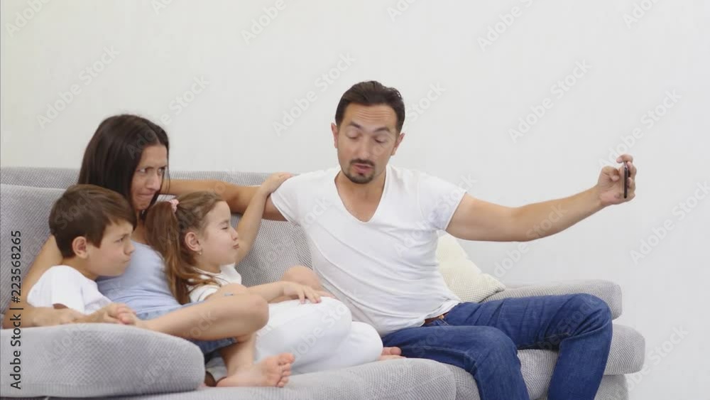 Cheerful family with children laughing taking selfie together on phone, young dad holding smartphone making photo of son and daughter at home, loving parents having fun with kids and gadget Cheerful family with children laughing taking selfie together on phone, young dad holding smartphone making photo of son and daughter at home, loving parents having fun with kids and gadget