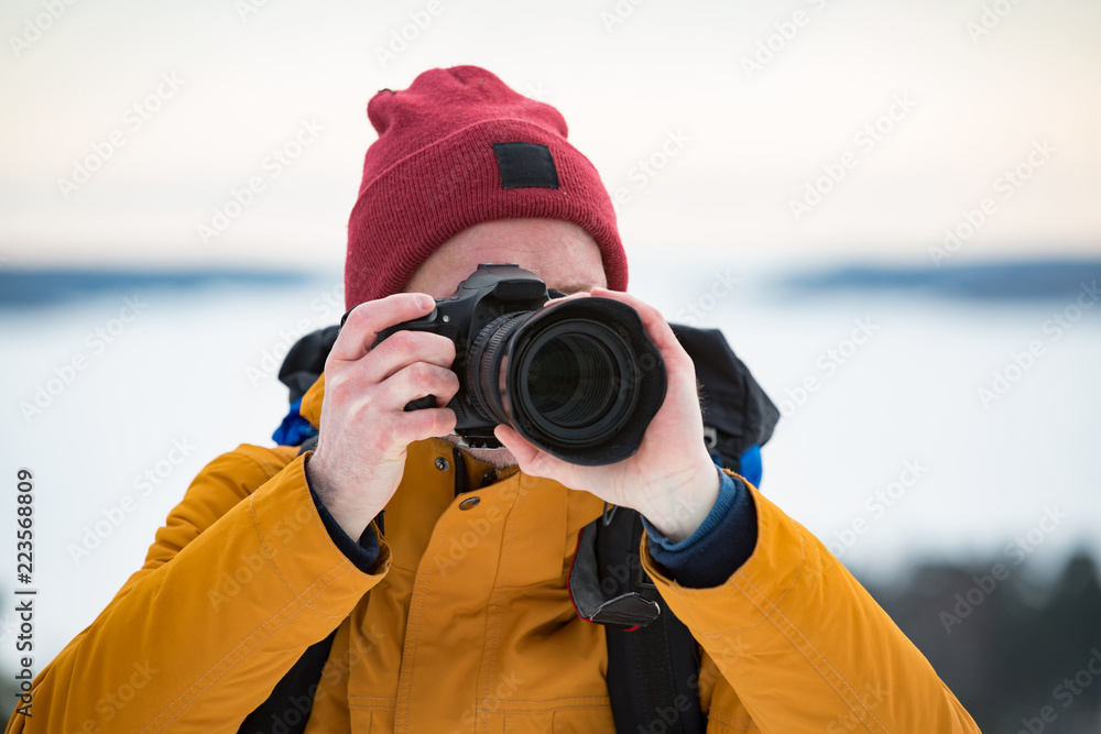 Obraz premium Portrait of mature man with grey beard exploring Finland in winter. Traveler Taking pictures on the top of rock. Beautiful view of northern landscape with frozen Baltic Sea and snowy islands.