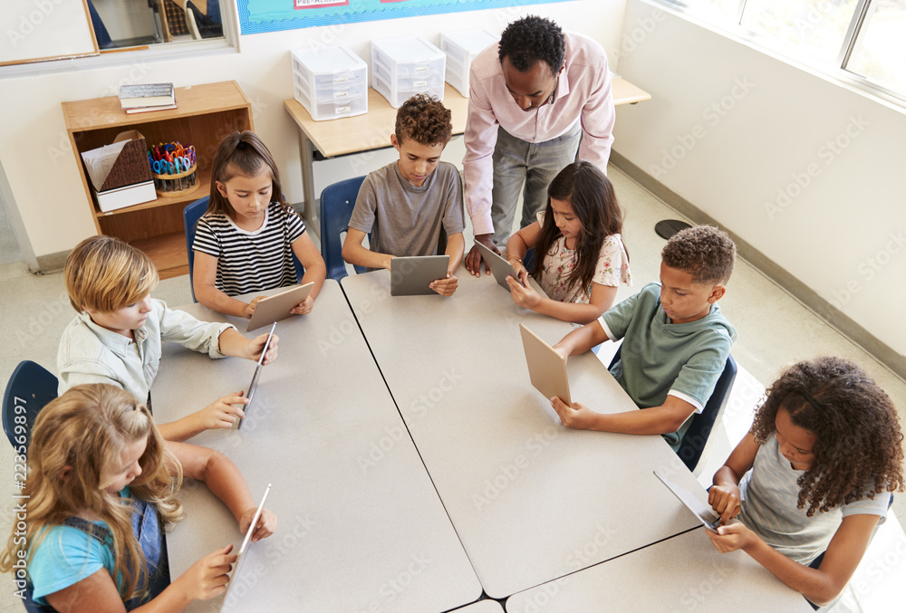 Fototapeta premium Teacher helping kids using tablets in lesson, elevated view