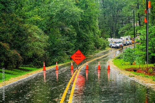 Fotografia An emergency road closure on a wet paved road after storm damage with utility trucks in the background