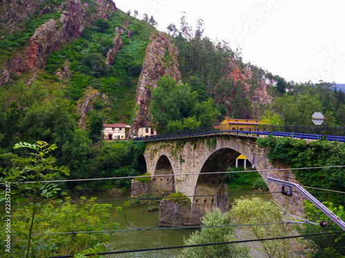 Stoned bridge crossing Nalon river between mountains, in Asturias, Spain