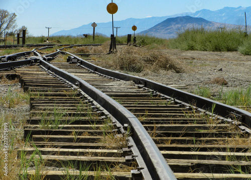 Historic narrow gauge railroad tracks run toward a switch junction and signals in an old rail yard in Laws, California in the Owens Valley with the Sierra Nevada mountains in the distance.. photo