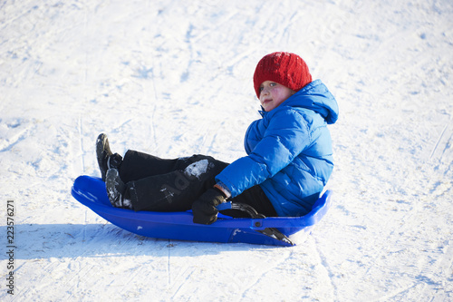 Child boy riding a bobsled. Having fun on the snow. Children winter activities.