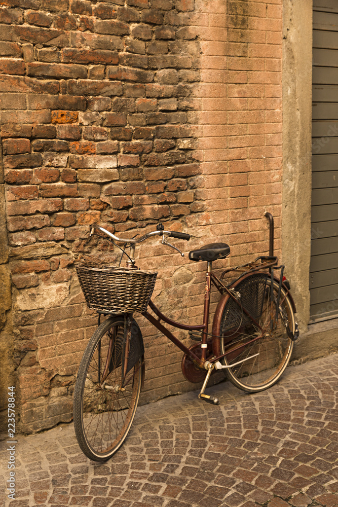 Bicicleta antigua con cesta sobre fachada de ladrillo antiguo.