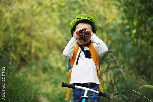 The little boy young researcher exploring with binoculars and backpack environment