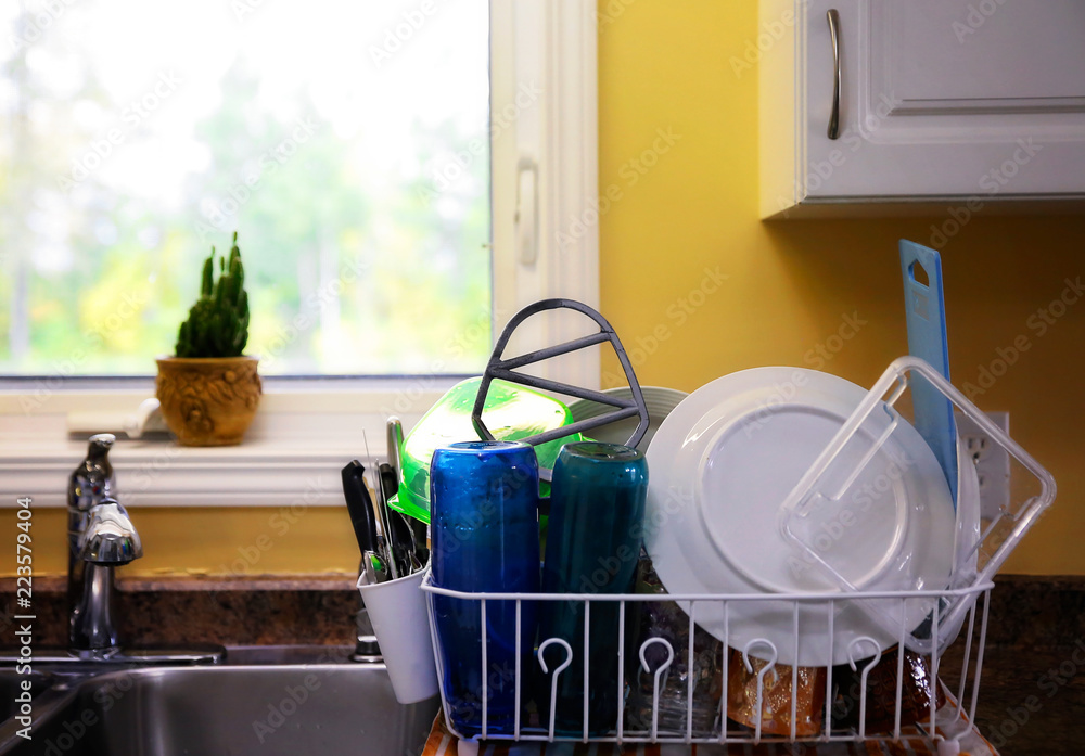 A plastic dish rack on a kitchen counter filled with washed dishes and  cutlery Stock Photo