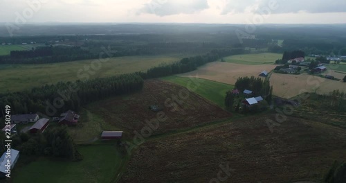 Drone rising above fields of wheat and other plants. Aerial quiet farm and forest scene in Finland during cloudy sunset. Uukuniemi. photo