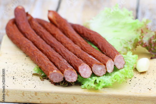 Traditional Polish smoked kabanos on lettuce on wooden board
