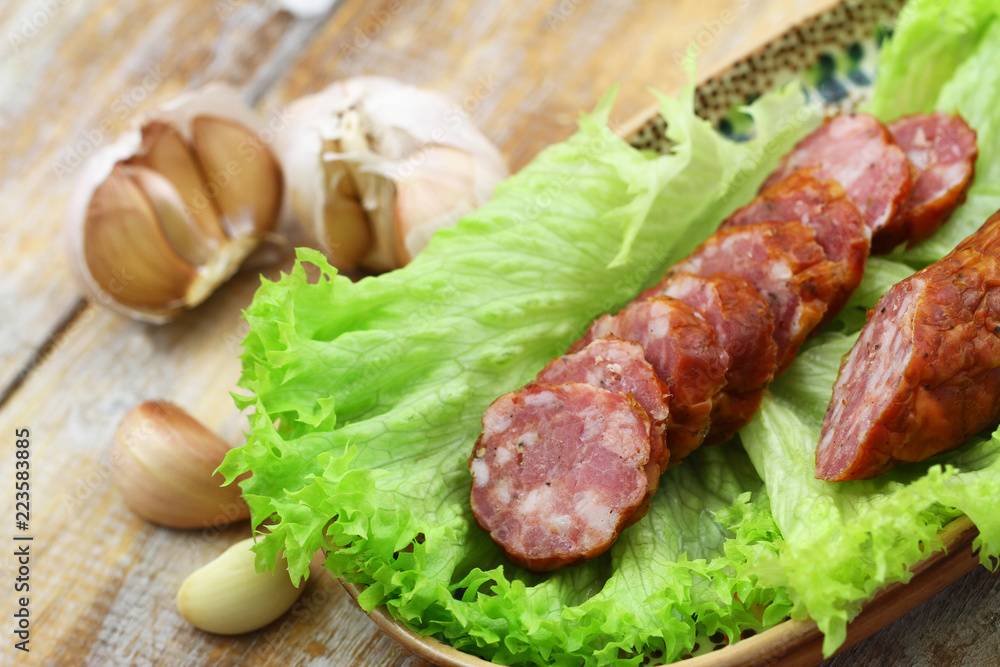 Slices of traditional smoked sausage on lettuce, closeup
