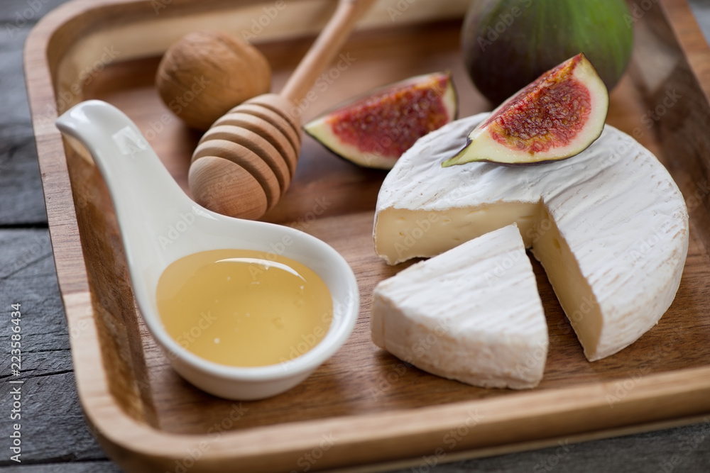 Close-up of a brown wooden serving tray with camembert cheese, honey and fig fruits, selective focus