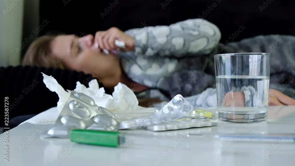 Slow motion of pills, thermometer and glass of water with young sick woman coughing heavily on background. Slow motion of pills, thermometer and glass of water with young sick woman coughing heavily on background.