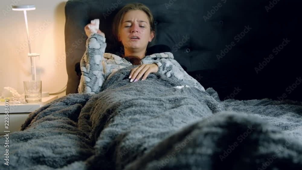 Young sick and tired woman with fever in bed blowing her nose and