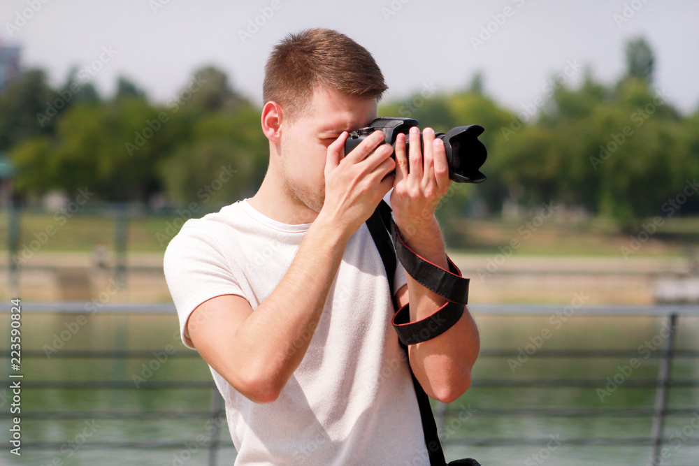 Professional photographer examining scenery and taking pictures of environment, architecture, urban elements, river, old green bridge. Tourist and traveler is making landscape photography with camera.