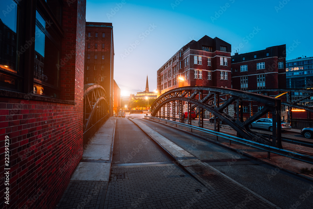 Obraz premium Empty Poggenmuehlen Bridge at twilight. Hamburg, Germany. illuminated buildings and last sunrays. Warehouse District -Speicherstadt Landmark of HafenCity quarter. Most visited touristic famous place