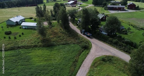 Aerial view of tractor driving forward in a sand road middle of a hay fields and farms during sunny summer day. Drone filming above and follows vehicle. Uukuniemi. Finland. Scandinavia. photo