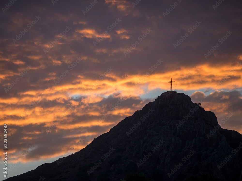 Orangener Sonnenuntergang über schwarzem Hügel mit Gipfelkreuz, Elba